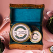Load image into Gallery viewer, Petrusco Amur and River Beluga Hybrid caviar tins nestled in a vintage brass chest with teal velvet lining, pink ribbon, and green velvet pouch.

