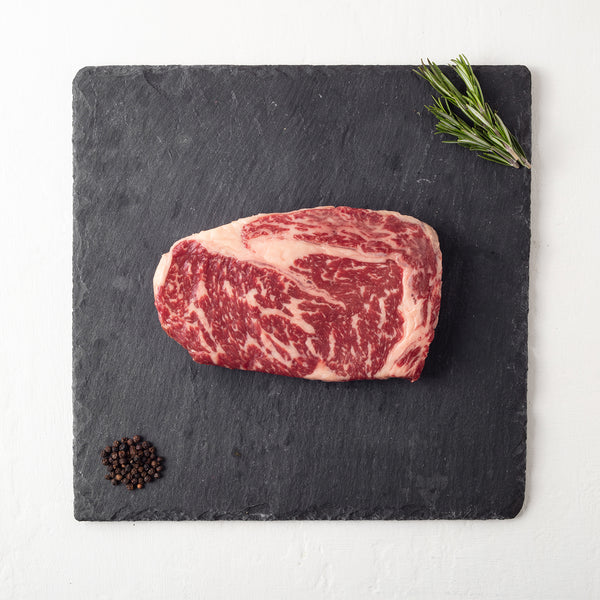 Raw steak on a slate board with rosemary and peppercorns