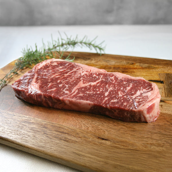 Raw steak on a wooden cutting board with herbs
