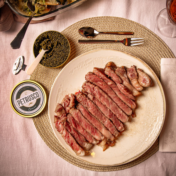 A jar of black Petrusco River Beluga caviar next to a cut steak