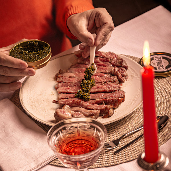 Someone spooning black caviar on a cut steak