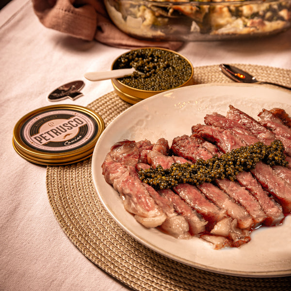 A spoon in a tin of Petrusco caviar next to caviar on a steak