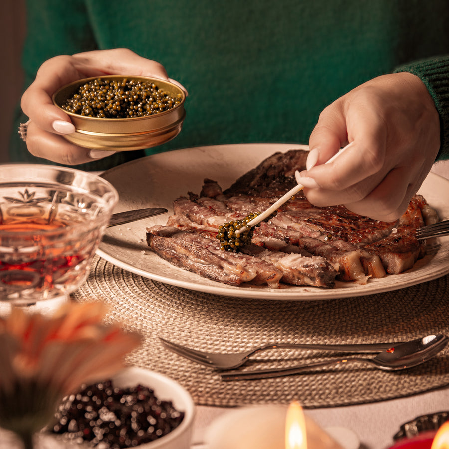Someone putting black caviar on a cut up steak