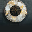 Load image into Gallery viewer, Blinis topped with crème fraîche and paddlefish caviar on a black slate plate with a spoon and extra blinis
