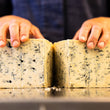 Load image into Gallery viewer, Person cutting a block of blue cheese with hands visible
