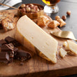 Load image into Gallery viewer, Cheese wedge on a wooden board with chocolate, nuts, and crackers.
