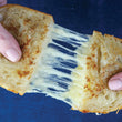 Load image into Gallery viewer, Close-up of a grilled cheese sandwich being pulled apart with a blue background
