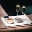 Load image into Gallery viewer, Petrusco caviar tin with champagne flutes, blueberries, crackers, and crème fraîche on a poolside tray.
