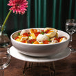 Load image into Gallery viewer, Petrusco Smoked Trout Roe tin on ice in a gold-rimmed glass bowl on a marble stand with mother-of-pearl spoons, pink flower, and green velvet backdrop.
