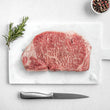 Load image into Gallery viewer, Petrusco Caviar fresh Japanese A5 Wagyu Striploin Steak on a marble cutting board with herbs,  fresh pepper, and salt.
