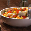 Load image into Gallery viewer, Close-up of potato and egg salad topped with salmon roe, peas, and tuna in a white bowl on a wooden table with crystal glasses

